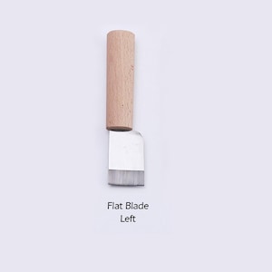 May include: A small, flat blade leather craft tool with a wooden handle. The blade is made of metal and has a slightly rounded edge. The handle is made of light brown wood. The text "Flat Blade Left" is printed below the tool.