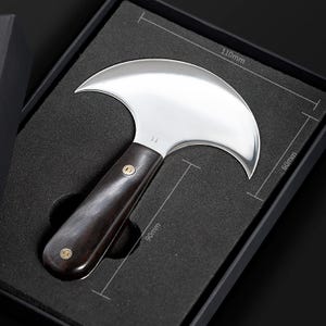 May include: A leatherworking knife with a curved, polished steel blade, 4.3 inches wide, and a dark wooden handle, 3.5 inches long. The knife is presented in a black box with dimensions marked as 110mm x 60mm x 90mm.
