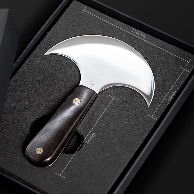 May include: A leatherworking knife with a curved, polished steel blade, 4.3 inches wide, and a dark wooden handle, 3.5 inches long. The knife is presented in a black box with dimensions marked as 110mm x 60mm x 90mm.