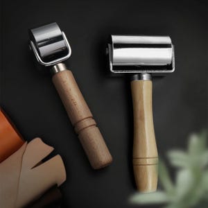May include: Two leather working tools with wooden handles and metal rollers. The rollers are used to smooth and flatten leather.