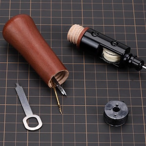 May include: A wooden spool with a black metal top and a small spool of thread. The spool is open and contains several needles. A small metal key is also included.