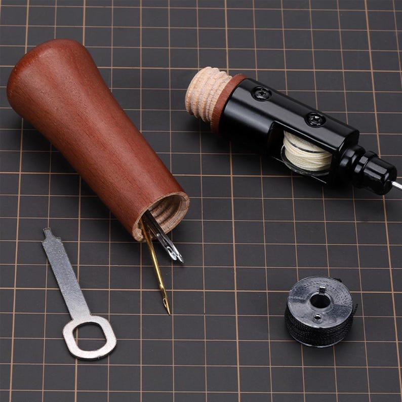 May include: A wooden spool with a black metal top and a small spool of thread. The spool is open and contains several needles. A small metal key is also included.