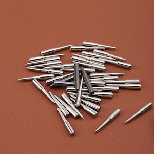 May include: A pile of silver and black metal sewing needles, some with pointed tips and some with rounded tips.