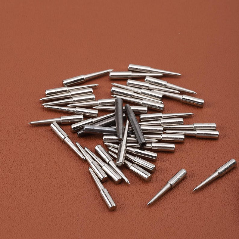 May include: A pile of silver and black metal sewing needles, some with pointed tips and some with rounded tips.