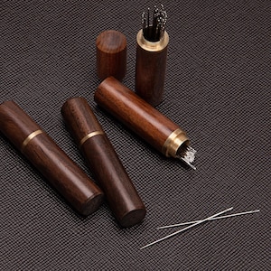 May include: A collection of wooden needle cases and a small container with needles. The cases are cylindrical with brass accents. The needles are silver and are scattered around the cases. The wood has a rich, dark brown color.