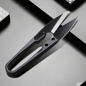 May include: Close-up of black thread snips with the word "EAGLE" printed on the handle. The blades are open, revealing a silver cutting edge. The snips are on a gray surface.