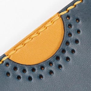 May include: Close-up of a blue leather wallet with a yellow stitched edge and a half-circle of decorative holes.