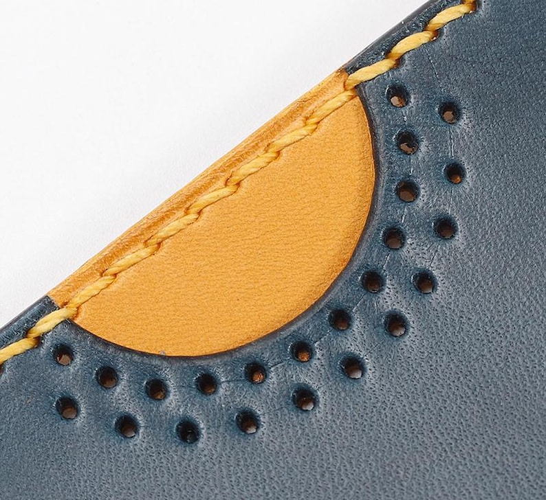May include: Close-up of a blue leather wallet with a yellow stitched edge and a half-circle of decorative holes.