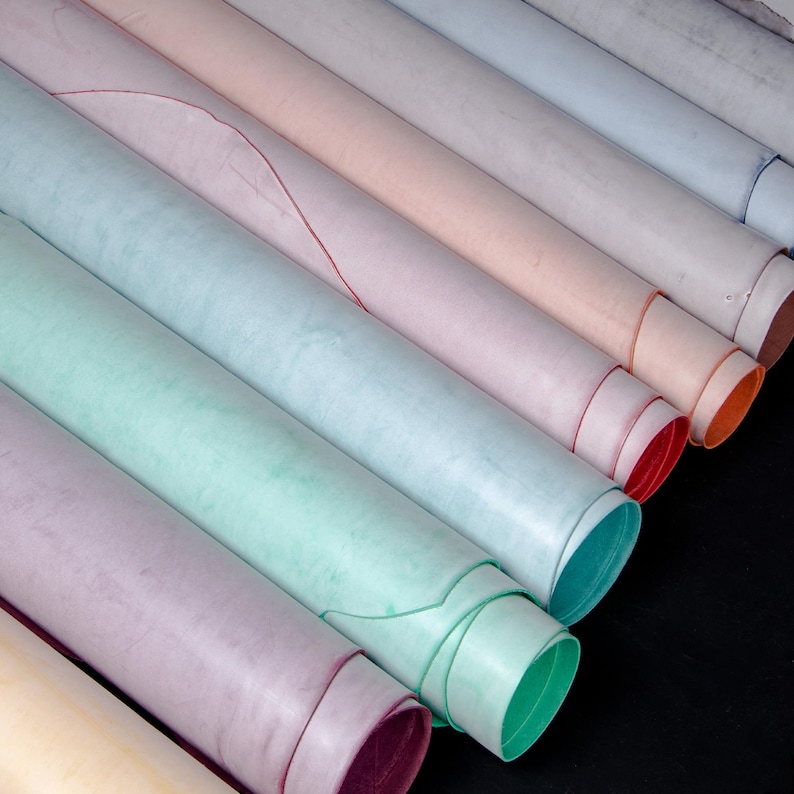 May include: A selection of rolled leather hides in pastel shades such as pink, blue, green, and purple. The edges of the rolls show the contrasting colours of the leather's interior. The hides are arranged diagonally, creating a visually appealing display.