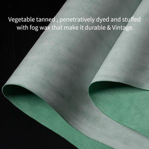 May include: A close-up shot of a piece of leather, showing a gray-green, textured surface. The underside is a bright green. Text at the top reads: "Vegetable tanned, penetratively dyed and stuffed with fog wax that make it durable & Vintage."