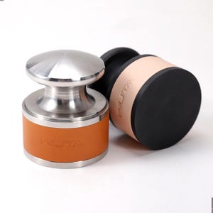 May include: Two leather and metal tools. One tool has a silver top and a tan leather band with the word "WUTA" embossed. The other tool is black with a tan leather band and the word "WUTA" embossed.