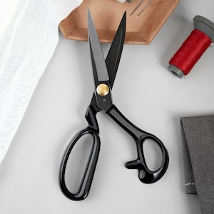 May include: Black fabric shears with gold accents and a 10 printed on the blade. The shears have a curved handle and a sharp blade.