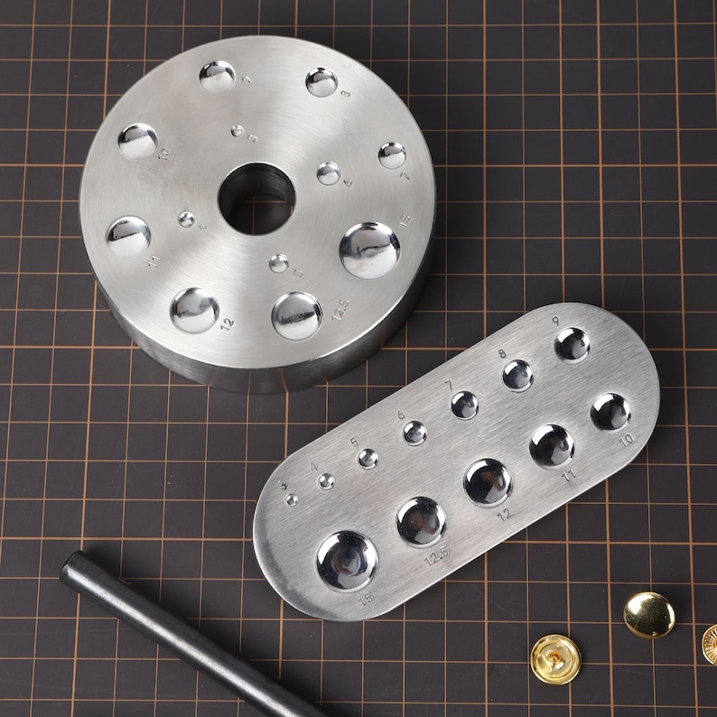 May include: Two metal tools for punching holes in leather. The larger tool is a round disc with a hole in the center and 12 different sized punch holes around the edge. The smaller tool is an oval shape with 10 different sized punch holes. Both tools are made of silver metal.