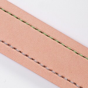 May include: Close-up of a section of light brown leather with two parallel lines of stitching. One line is stitched with light green thread, and the other with light grey thread. The leather has a slightly textured surface.