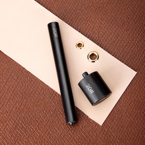 May include: Black leather hole punch set with a handle and a punch tool. The tools are labeled "20#" and there are three gold metal eyelets.