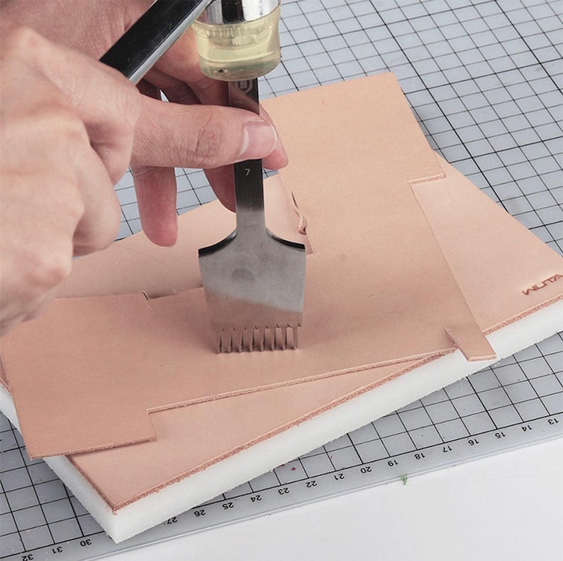 Puede incluir: Una persona usando una herramienta de costura de cuero para perforar agujeros en un trozo de cuero. La herramienta tiene un mango y una cabeza de metal con m&uacute;ltiples p&uacute;as. El cuero se coloca sobre una estera de espuma blanca con un patr&oacute;n de cuadr&iacute;cula.