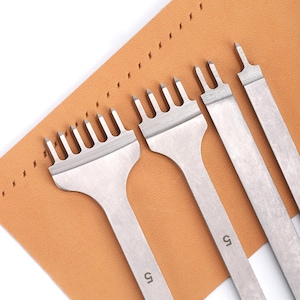 May include: Four leather craft tools with different sized stitching punches. The tools are made of metal and have a brown leather background.