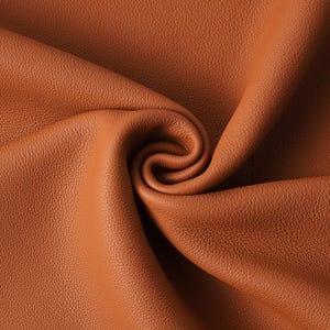 May include: Close-up of a swatch of brown leather with a textured surface. The leather is folded and curled, creating a spiral pattern. The color is a warm, medium brown.