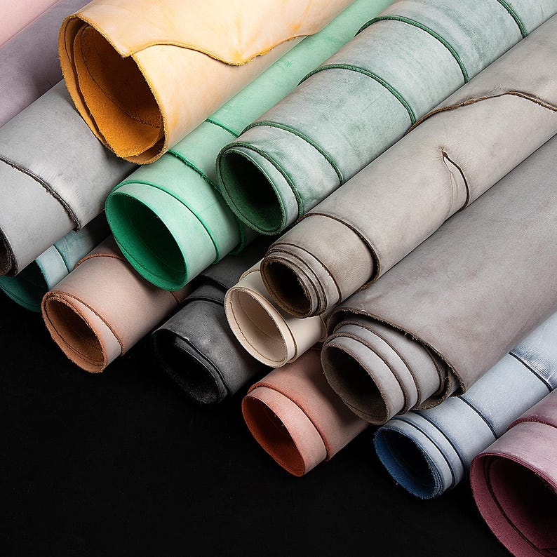 May include: A selection of rolled leather hides in shades of grey, green, pink, and yellow. The edges of the leather are visible, displaying the different colours and textures. The hides are arranged diagonally, creating a visually appealing arrangement.