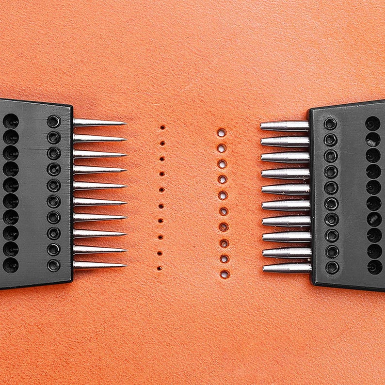 May include: Two black leather stitching tools with rows of needles on a brown leather surface. The tools are used to create evenly spaced holes in leather for stitching.