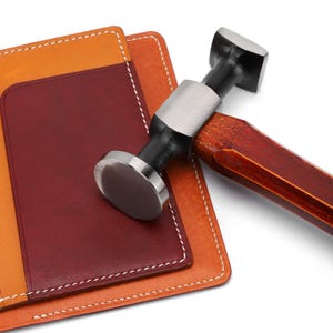 May include: A leather wallet with a red and orange interior and a wooden handled hammer with a metal head.