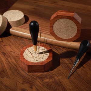 Puede incluir: Una colecci&oacute;n de herramientas y accesorios para carpinter&iacute;a. La imagen presenta un port agujas de madera con agujas, una lezna de madera y un posavasos de madera. Los art&iacute;culos son de madera y tienen un acabado natural. Las herramientas est&aacute;n dispuestas sobre una superficie de madera.