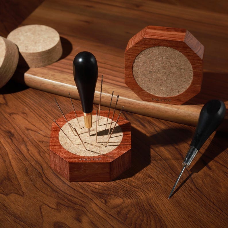 Puede incluir: Una colecci&oacute;n de herramientas y accesorios para carpinter&iacute;a. La imagen presenta un port agujas de madera con agujas, una lezna de madera y un posavasos de madera. Los art&iacute;culos son de madera y tienen un acabado natural. Las herramientas est&aacute;n dispuestas sobre una superficie de madera.