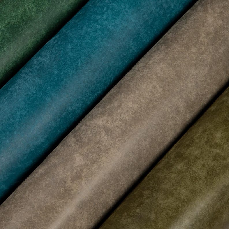 May include: Close-up of four rolls of textured fabric in shades of green, teal, and brown. The fabric has a distressed, weathered appearance, with variations in color and texture. The rolls are angled diagonally across the frame.