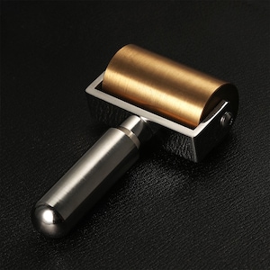 May include: A silver and brass roller tool with a handle. The roller is made of brass and has a smooth, shiny surface. The handle is made of silver and has a textured surface.