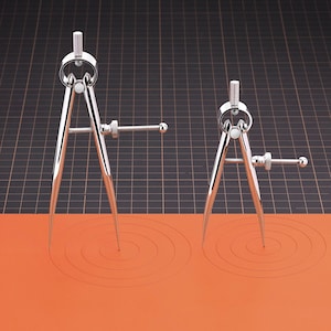 May include: Two silver compasses with adjustable points are shown on a black and orange surface. The compasses are used to draw circles.