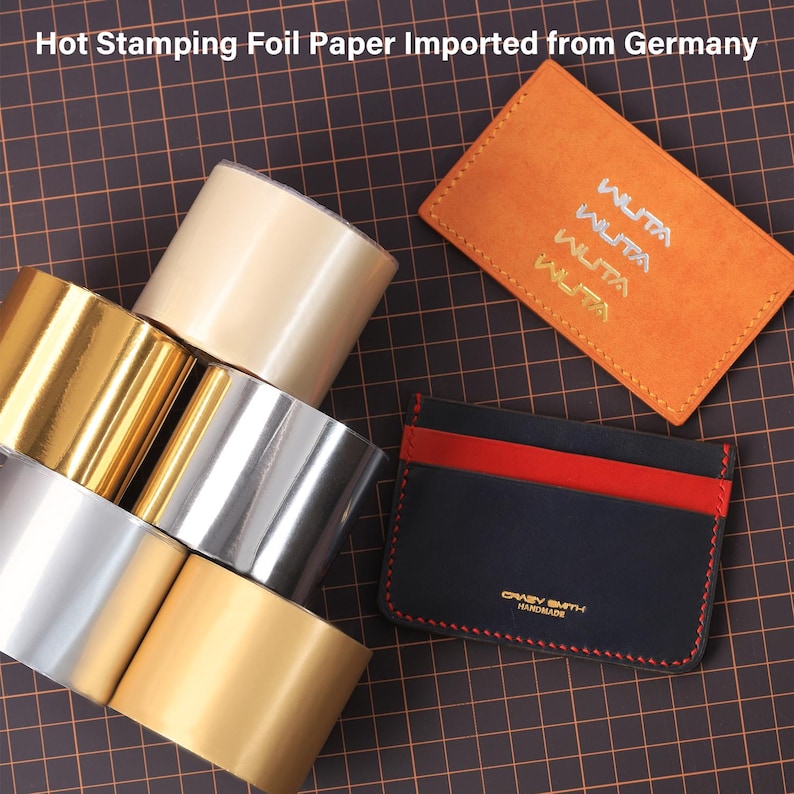 May include: Assortment of metallic hot stamping foil rolls in gold, silver, and beige, alongside two leather cardholders. One cardholder is orange with "WUTA" text, the other is navy with a red stripe and "CRAZY SMITH HANDMADE" text.