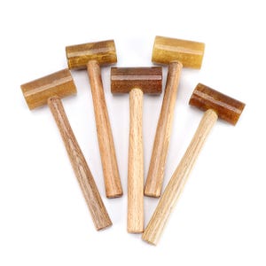 May include: A collection of small wooden mallets with light brown handles and rectangular heads in varying shades of brown. The mallets are arranged on a white background, showcasing their natural wood grain and craftsmanship.