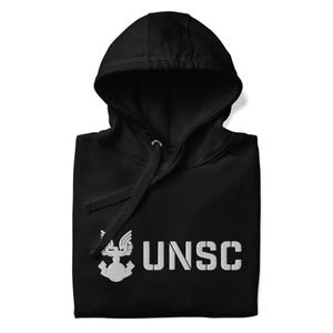 Può includere: Felpa con cappuccio nera con testo "UNSC" bianco e un emblema bianco sul davanti. La felpa con cappuccio ha un cordino e un cappuccio. La felpa è piegata ordinatamente.
