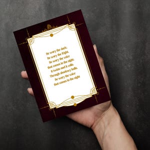 Pode incluir: Um cart&atilde;o bord&ocirc; com bordas decorativas douradas e texto. O texto diz: "Cuidado com a escurid&atilde;o. Cuidado com o susto. Cuidado com a voz que vem &agrave; noite. Ela se contorce e chama. Atrav&eacute;s de corredores sombrios."