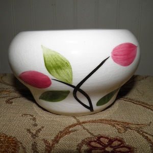 May include: White ceramic bowl with a floral design. The bowl has a rounded shape and features pink and green painted leaves and stems.