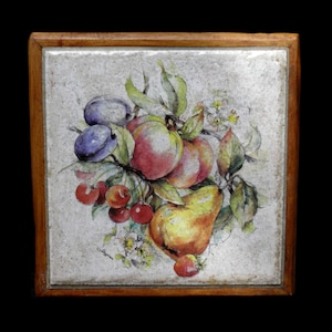 May include: Square wooden trivet with a hand-painted fruit still life. The artwork features plums, cherries, peaches, and a pear, with green leaves and white blossoms. The trivet has a light gray background and a dark brown wooden frame.