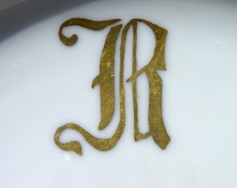 May include: A gold-colored letter R in a decorative script font on a white background.