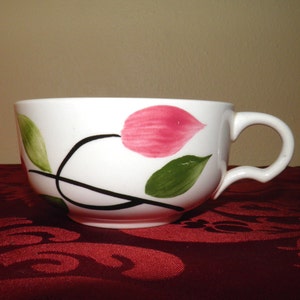 May include: White ceramic teacup with a black stem and pink and green floral design.