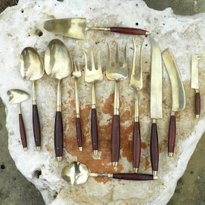 May include: A set of 10 brass serving utensils with wooden handles. The set includes a serving spoon, a serving fork, a cake server, a butter knife, and other utensils.