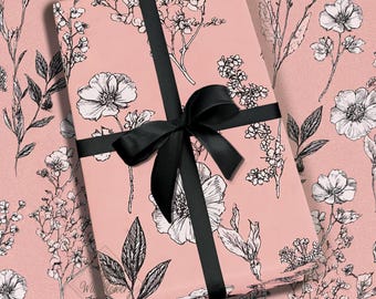 May include: A wrapped gift with a black ribbon and bow. The wrapping paper is light pink with a floral pattern in black and white. The gift is centered and the bow is tied on top.