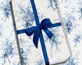 May include: A wrapped gift with a white background and a blue floral pattern. The gift is tied with a navy blue ribbon and bow. The wrapping paper features bouquets and bows in a classic toile design.