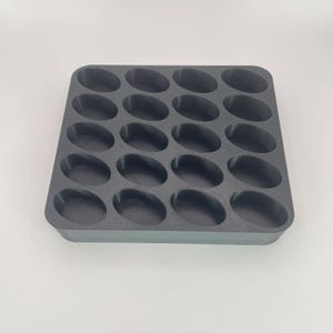 May include: A dark gray, rectangular mold with 20 oval-shaped cavities. The mold is designed for creating multiple small, uniform items. The cavities are evenly spaced and have rounded edges. The overall design is simple and functional.