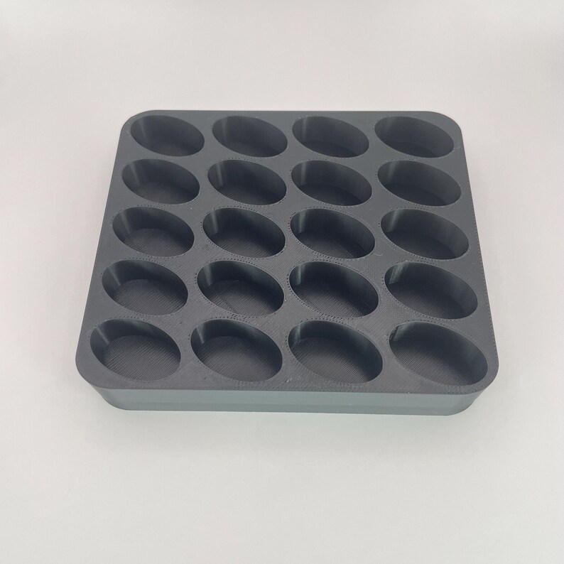 May include: A dark gray, rectangular mold with 20 oval-shaped cavities. The mold is designed for creating multiple small, uniform items. The cavities are evenly spaced and have rounded edges. The overall design is simple and functional.