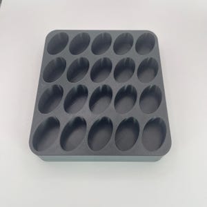 May include: A dark gray, rectangular organizer with 24 oval-shaped compartments. The organizer is made of a solid material and is designed to hold small items. The compartments are evenly spaced and have rounded edges.