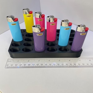 Pode incluir: Seis isqueiros BIC coloridos em azul claro, amarelo, rosa, magenta e roxo, cada um com topo de metal prateado e bot&atilde;o de igni&ccedil;&atilde;o vermelho, dispostos numa bandeja de pl&aacute;stico preta ao lado de uma r&eacute;gua com 19 cm de comprimento.