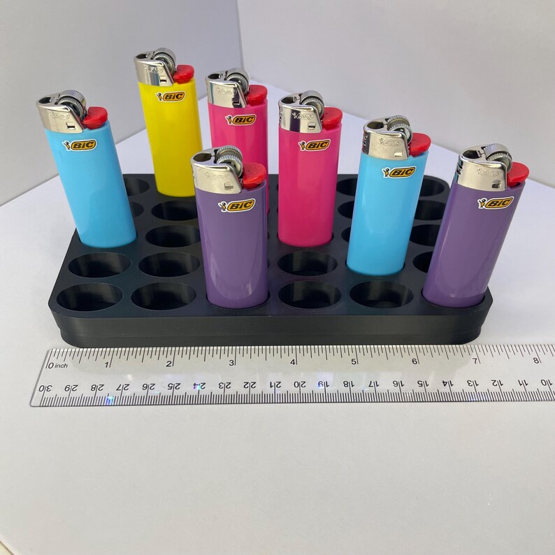 Pode incluir: Seis isqueiros BIC coloridos em azul claro, amarelo, rosa, magenta e roxo, cada um com topo de metal prateado e bot&atilde;o de igni&ccedil;&atilde;o vermelho, dispostos numa bandeja de pl&aacute;stico preta ao lado de uma r&eacute;gua com 19 cm de comprimento.