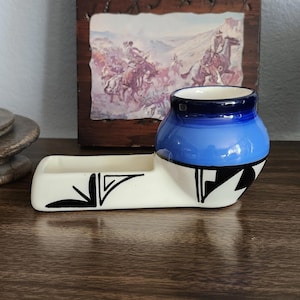 Może przedstawiać: Ceramiczna popielniczka z niebiesko-białym wzorem. Popielniczka ma małą, okrągłą miseczkę i prostokątną tacę. Miseczka jest niebieska z ciemnoniebieską obwódką. Taca jest biała z czarnymi geometrycznymi wzorami.