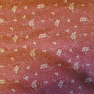 May include: Burgundy fabric with a repeating pattern of white floral sprigs and tiny white dots. The floral design includes leaves and bell-shaped flowers. The fabric has a slightly textured appearance.