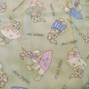 May include: Light green fabric with repeating cartoon bunny illustrations in pastel colors. The bunnies wear dresses and overalls. Text includes "Grow giggles", "Harvest love", and "Plant smiles".