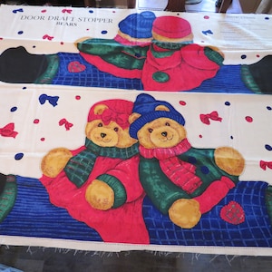 May include: A fabric panel featuring a repeating pattern of cartoon bears designed to be door draft stoppers. The bears wear red coats, blue sweaters, and hats, with green and red scarves. The background is white with red and blue accents.